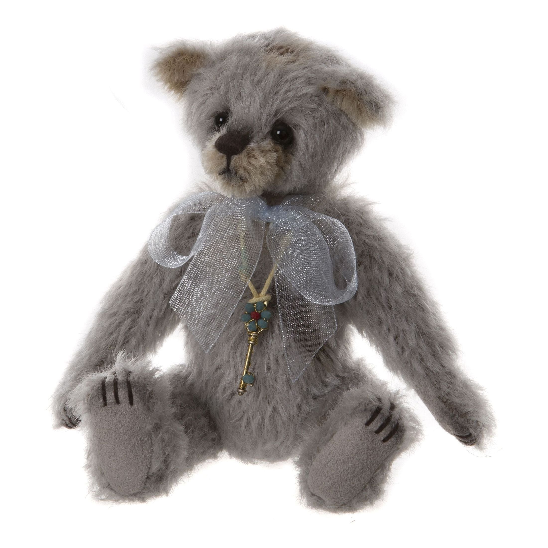 This is Little Boy Blue by Charlie Bears. This bear has a shaggy, long-pile coat that appears slightly wiry with a low sheen. The coat colours are gray and beige. The muzzle and inner ears are beige while the rest of the head, body and tummy are gray; the paw soles are a darker gray felt and the paw toes are indicated with dark stitched slashes. The eyes are glossy black plastic or glass and the nose is a dark brown/black stitched nose. There are no other fur markings. The bear is seated. It wears a la...