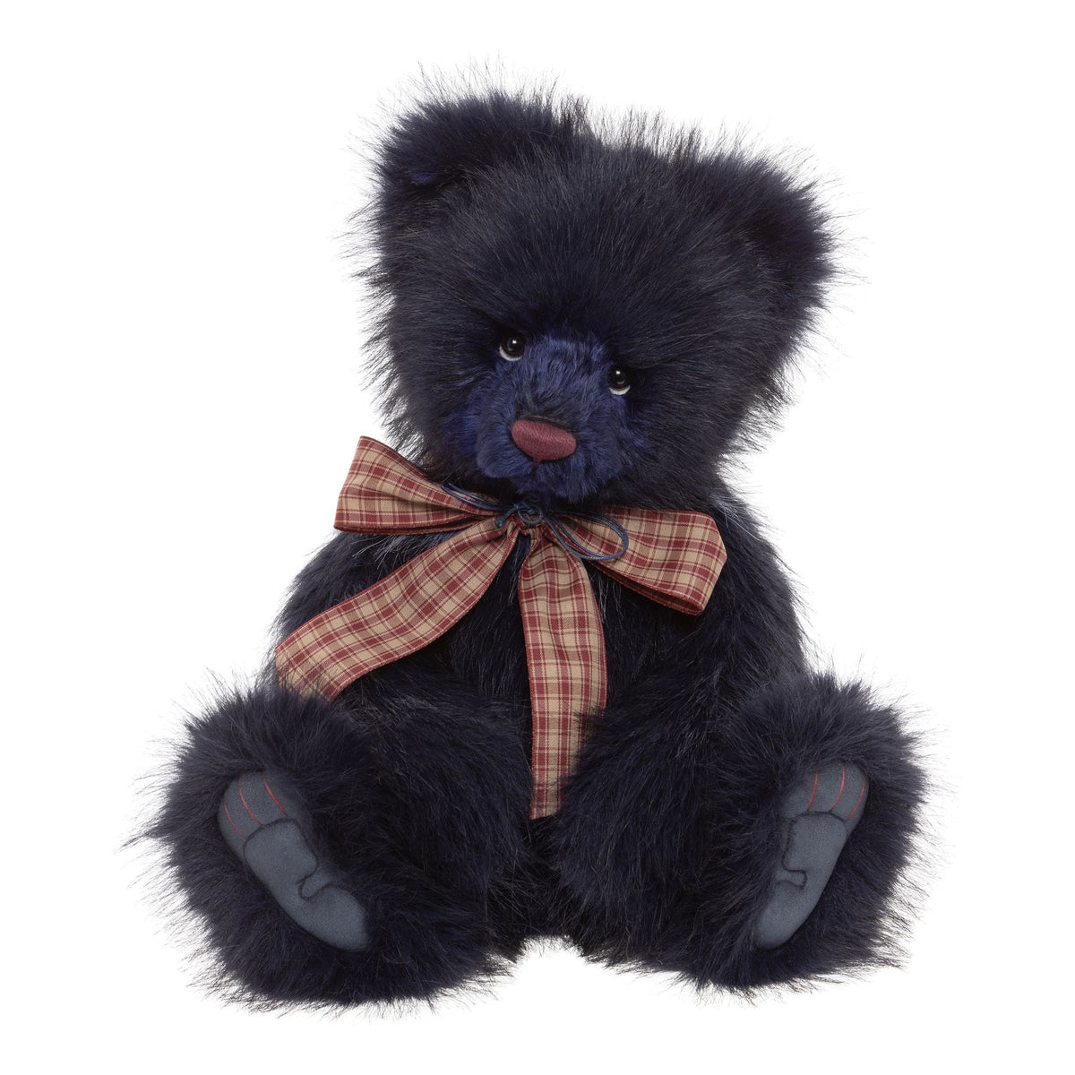This is Indigo by Charlie Bears. They have a deep navy, long-pile coat with a shorter, bright blue muzzle and face. Their paw pads and inner paws are gray and they wear a large red-and-beige checked bow around the neck. They have a soft, warm expression with glossy eyes and a slightly vintage character.