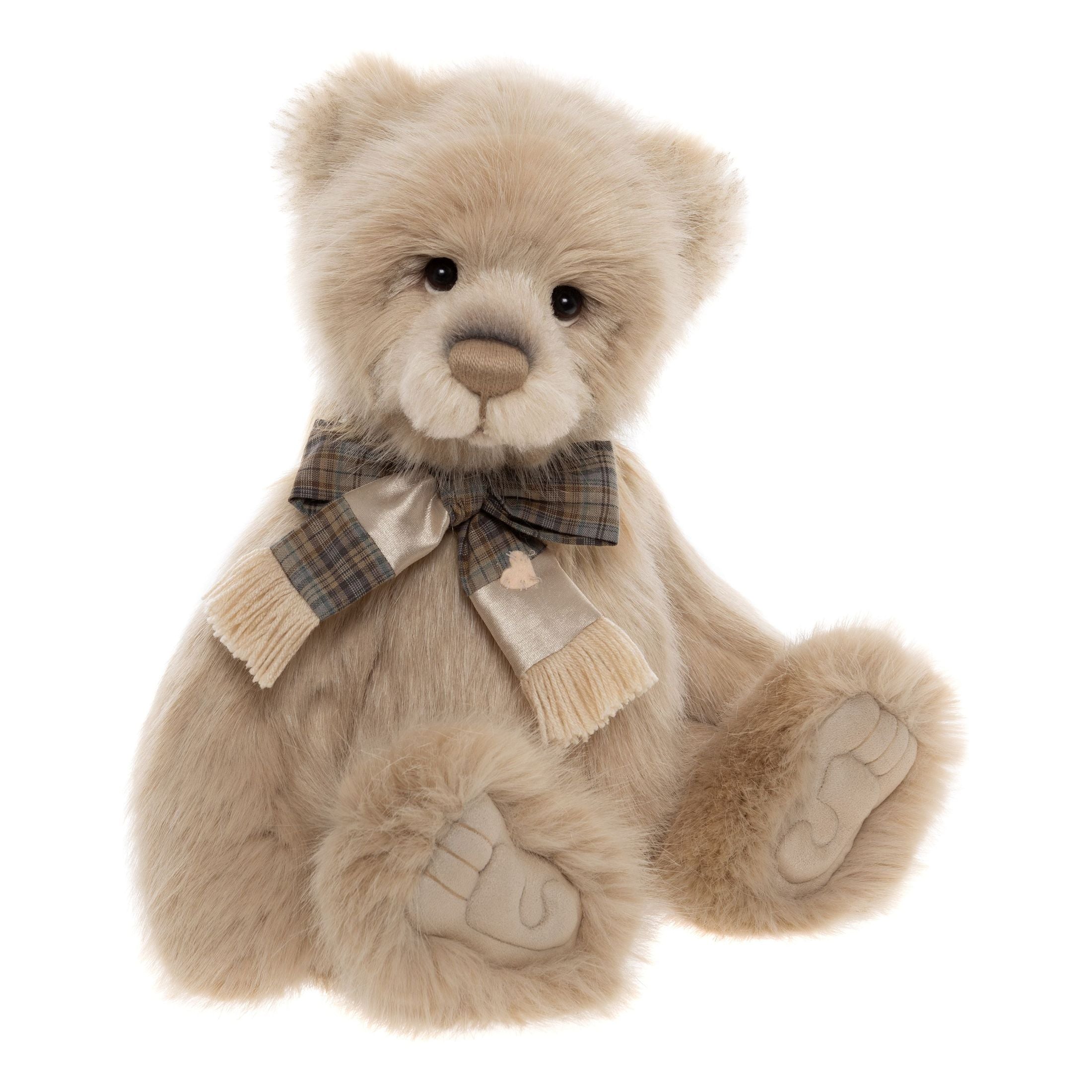 This is Jakub by Charlie Bears. He has a long, soft beige coat with a plush, silky pile. His muzzle and inner ears are lighter beige with a stitched brown nose, and his paw pads are beige suede; a checked scarf and a satin gold bow ribbon are tied at his neck. He has a gentle, slightly wistful expression.